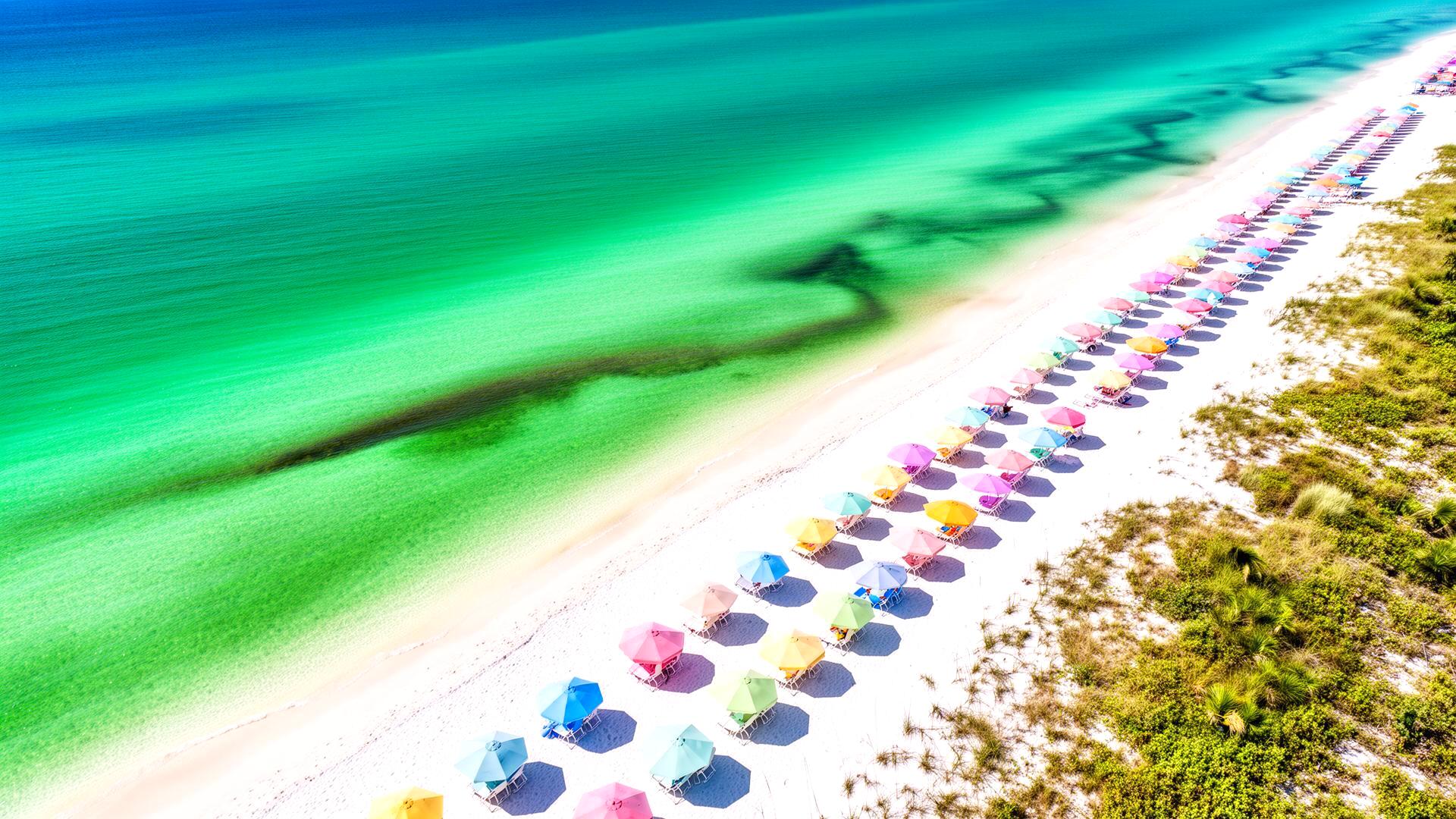 Aerial view of 30A's emerald Gulf waters and pastel beach umbrellas lining the sugar-white sand